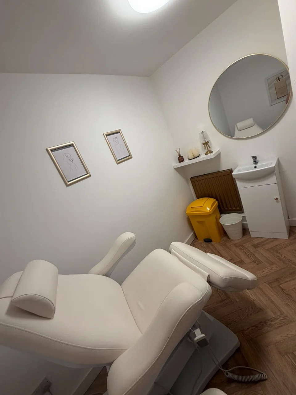 Treatment room with a reclining chair, round gold-framed mirror and washbasin